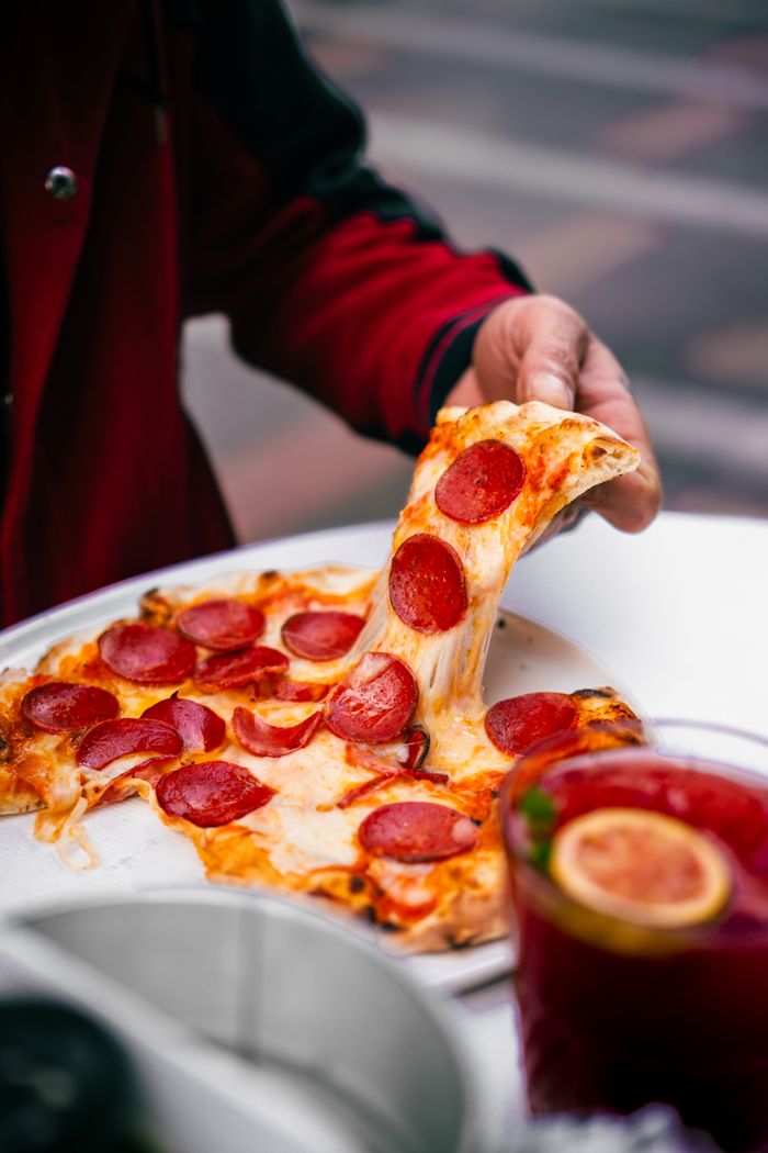 about-us-02 Close-up of a hand pulling a cheesy pepperoni pizza slice, perfect for food lovers.