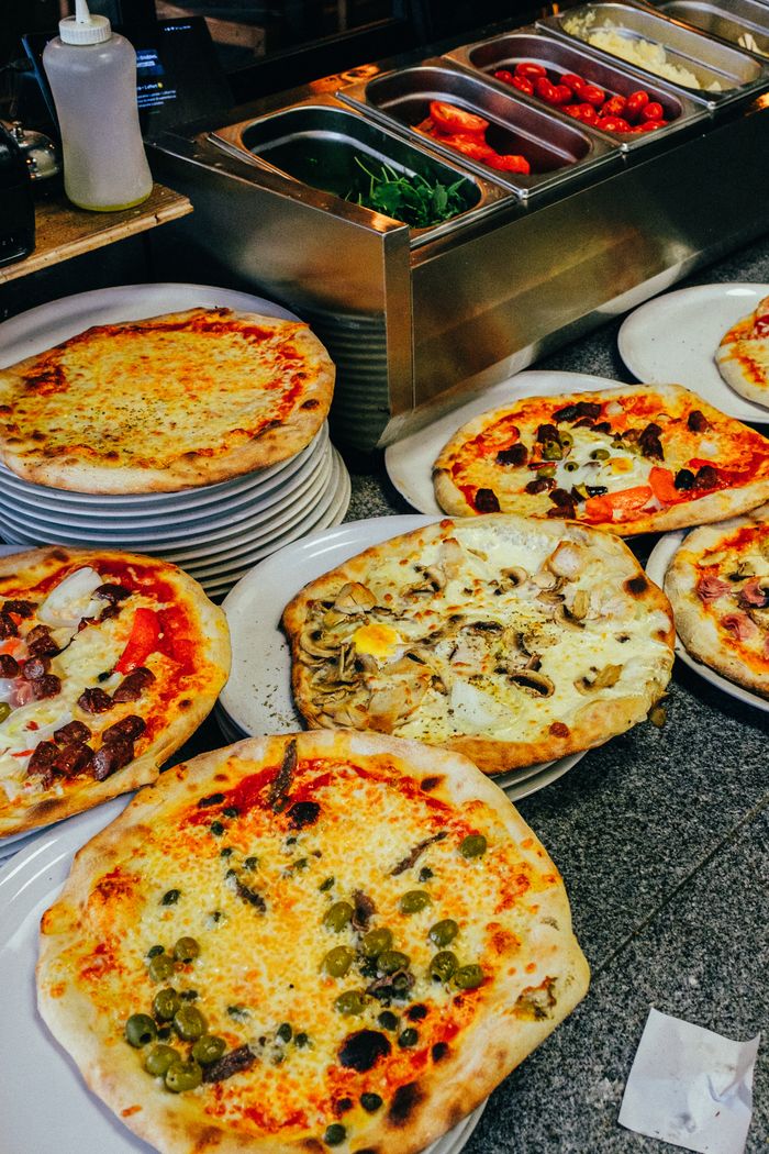 about-us-02 Multiple freshly baked pizzas displayed in a restaurant setting, showcasing assorted toppings.